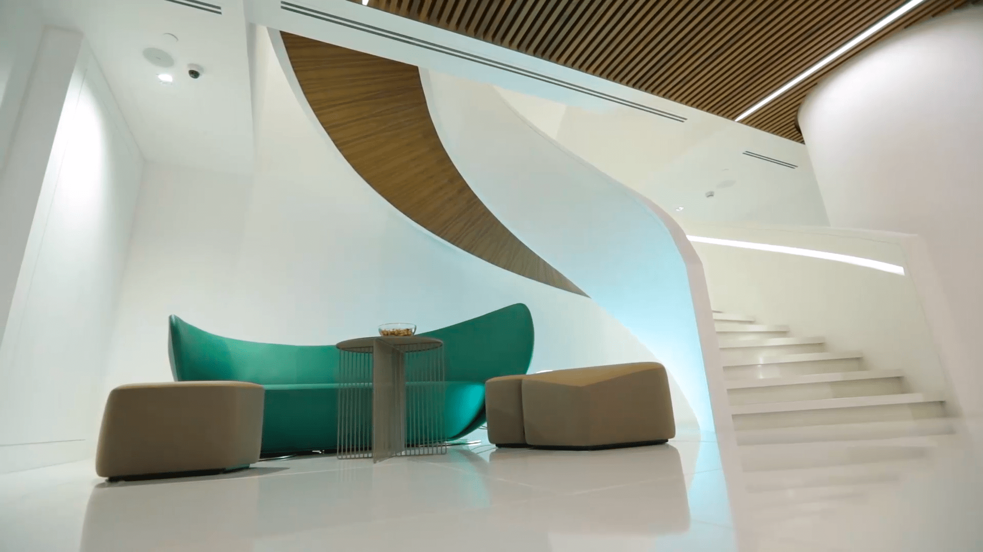 A futuristic interior with a curved green sofa, beige ottomans, dynamic architectural lines, and a sleek staircase.