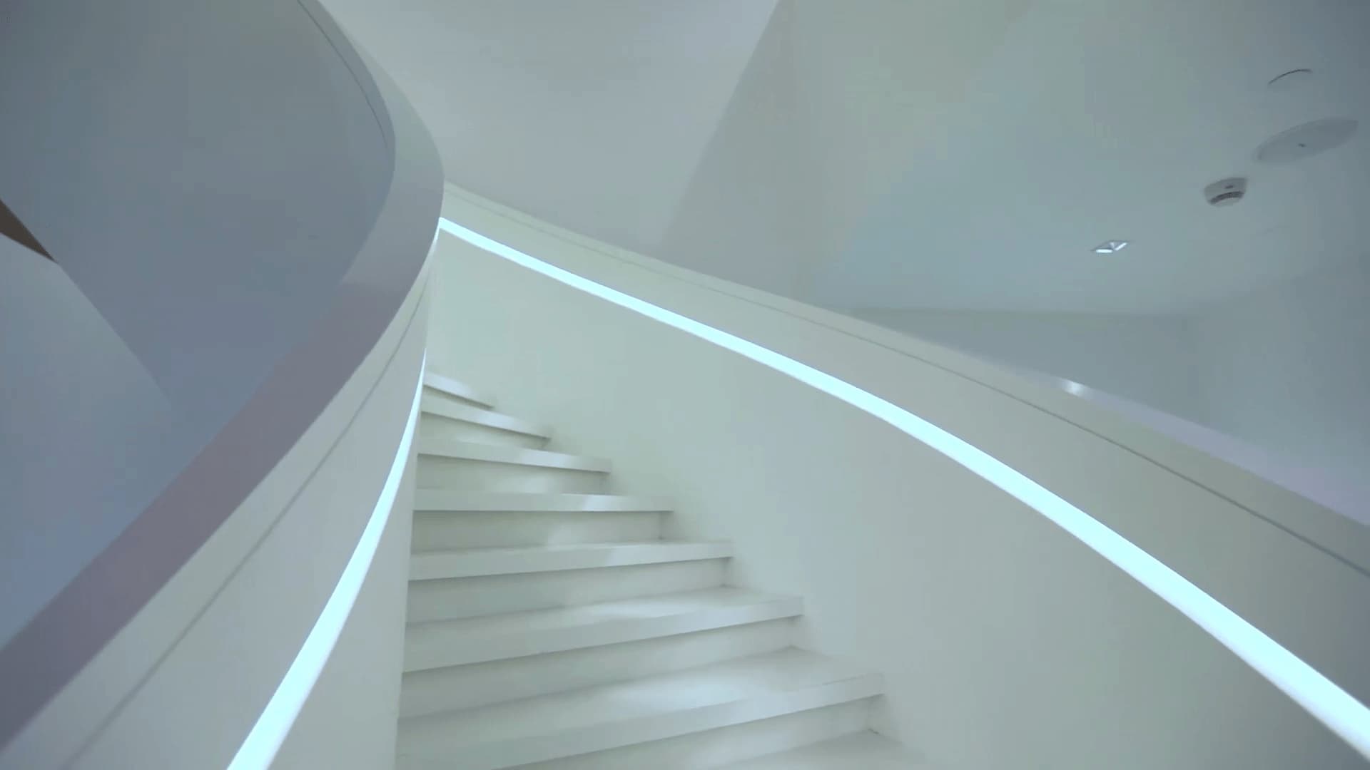 A modern staircase with white walls and steps, featuring sleek LED strip lighting along the wall edges.