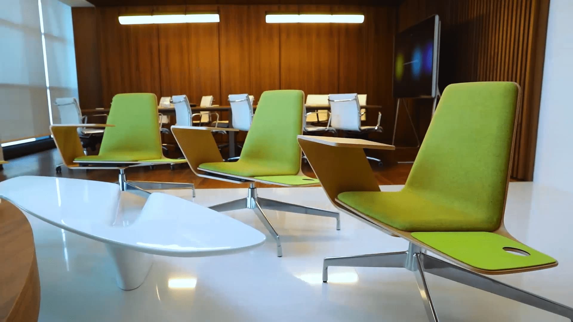 A modern conference room with bright green chairs, a sleek white table, warm wood paneling, and contemporary lighting.