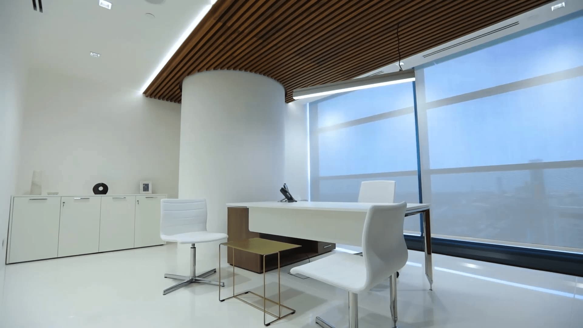 A modern office space with a clean white design, sleek furniture, wooden ceiling accents, and large windows for ample natural light.