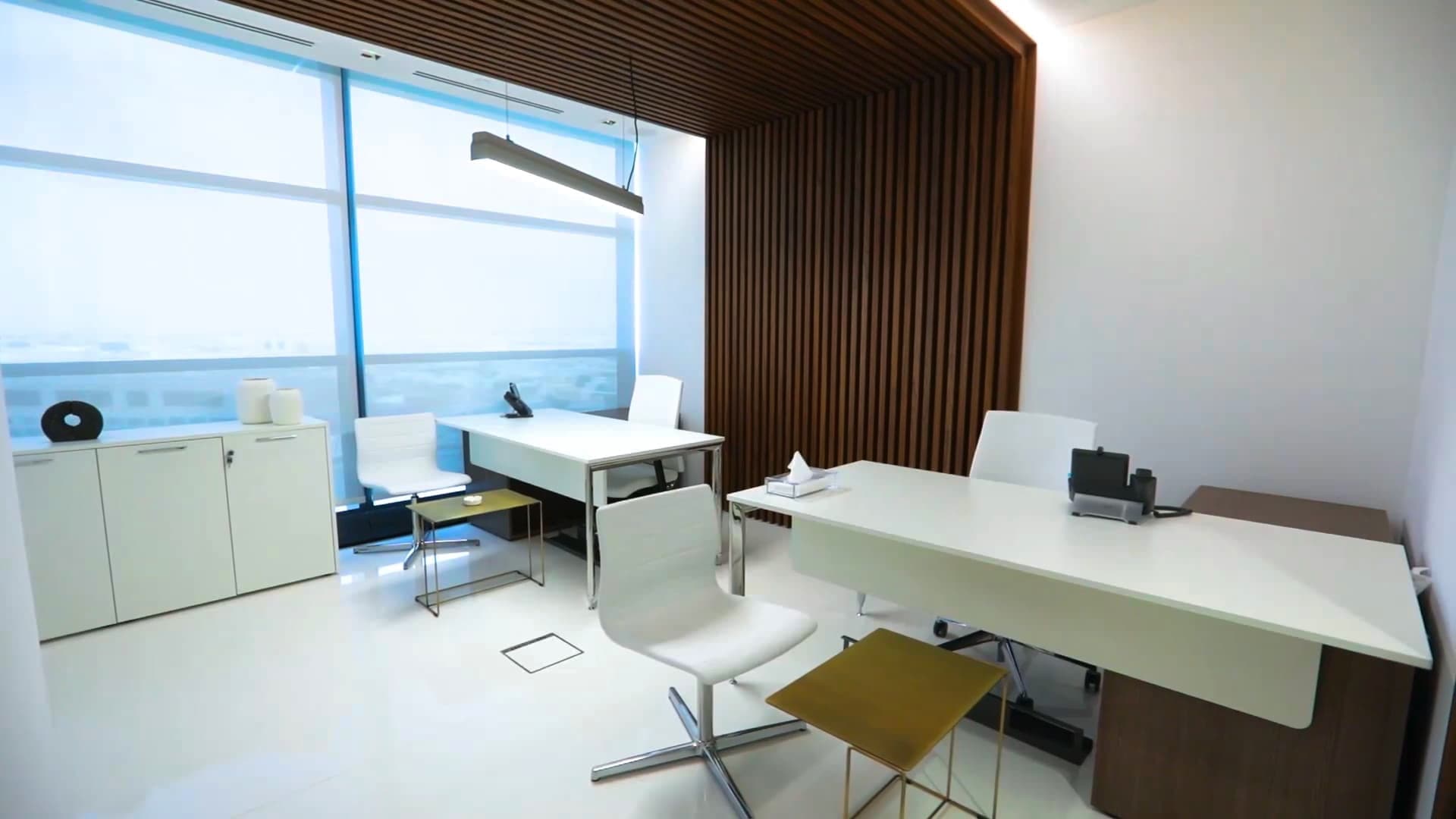 An office with white desks, wooden paneling, and a large window with a view.